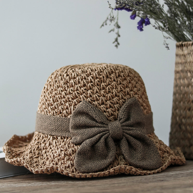 Vintage Foldable Straw Sun Hat with Wide Brim Bow displayed on a wooden table with flowers in the background.