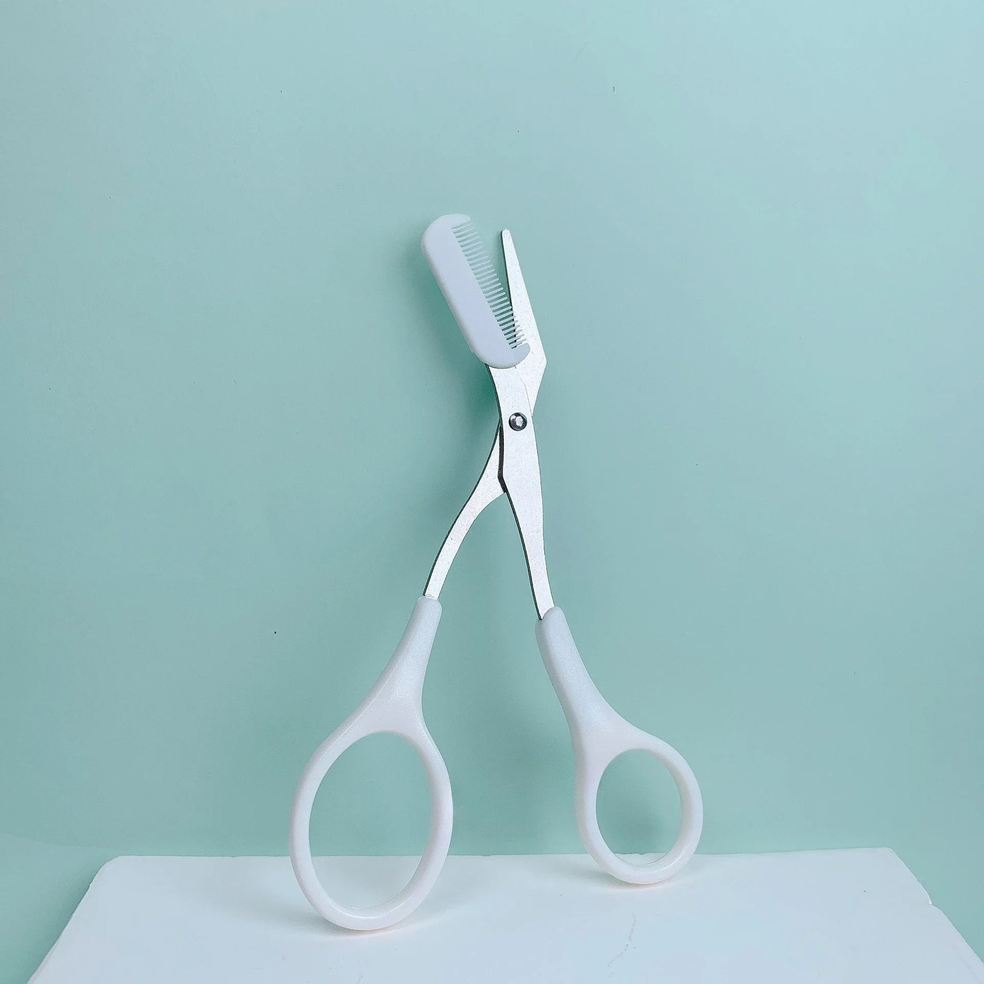 Eyebrow Trimming Scissors with Built-in Comb resting on a light blue background, showcasing its grooming design.