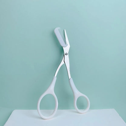 Eyebrow Trimming Scissors with Built-in Comb resting on a light blue background, showcasing its grooming design.