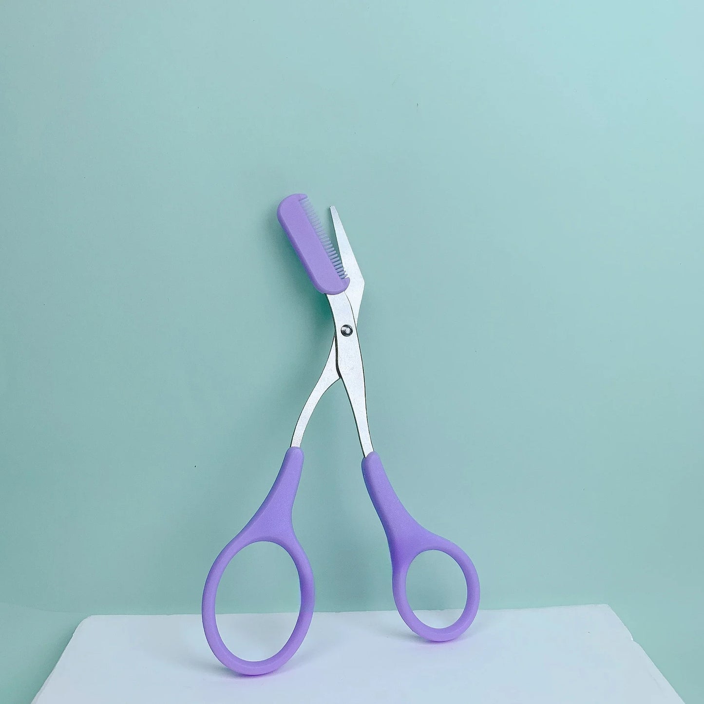 Eyebrow Trimming Scissors with Built-in Comb displayed on a light background, featuring purple handles and precision blades.
