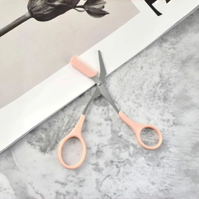 Eyebrow Trimming Scissors with Built-in Comb on a light background next to a magazine, showcasing its sleek design.