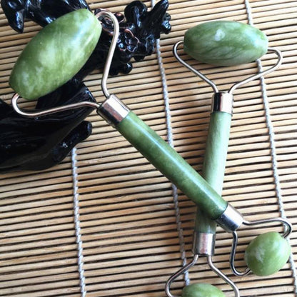 Double Head Jade Face Massage Roller resting on a bamboo mat, showcasing its jade texture and metal handles.